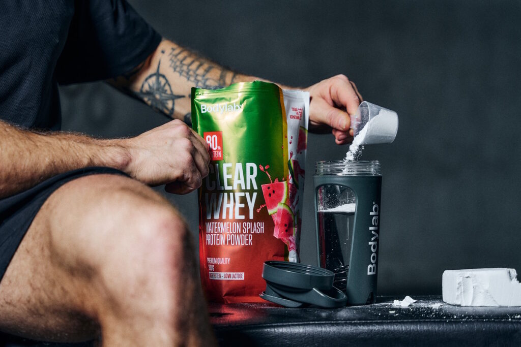 Henkilö annostelee Clear Whey -proteiinijauhetta shakeriin ennen juoman sekoittamista