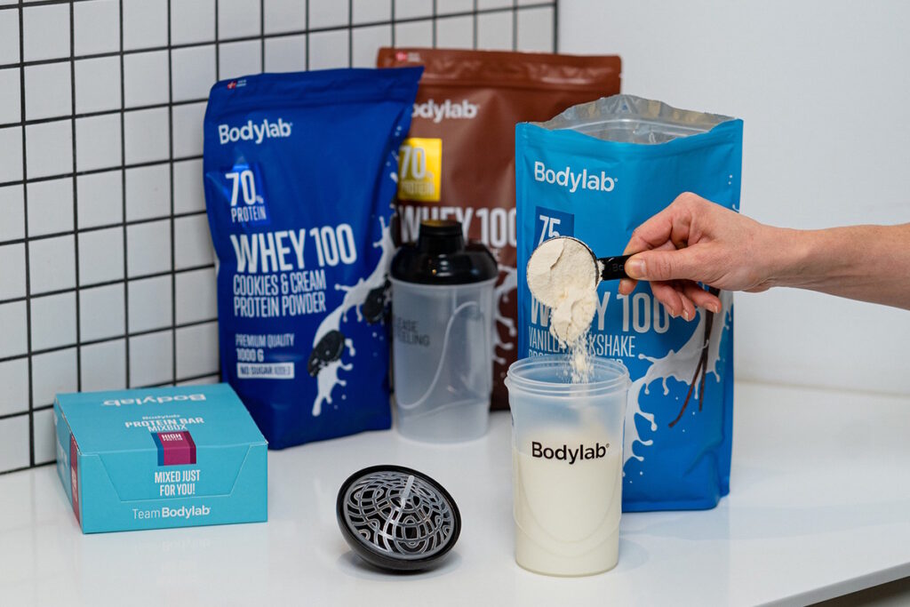 Whey 100 -proteiinijauheiden eri makuvaihtoehtoja pöydällä ja annostelu shakeriin